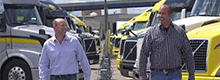 thumbnail of two men standing in a semi parking lot